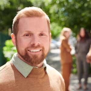 Handsome bearded college teacher Portrait of smiling handsome young bearded college teacher in sweater standing against campus